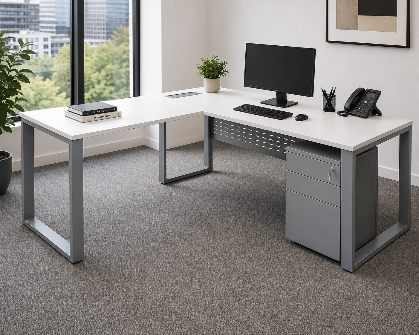 Modern office desk with computer setup in a bright room with large windows.